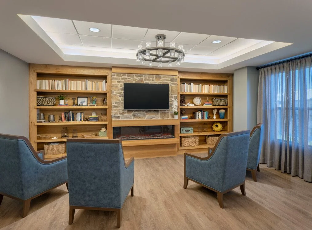 rustic and elegant community lounge and entertainment area with accent chairs, electric fireplace, and large television at Querencia