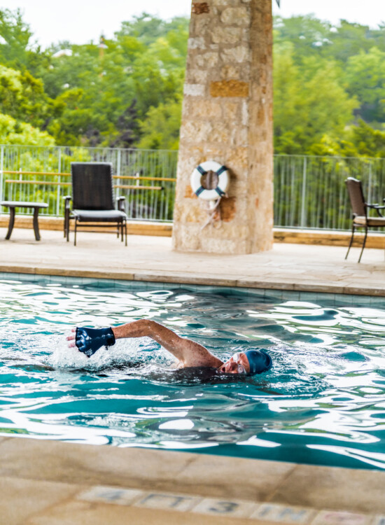 senior man in swim cap swims laps in the beautiful outdoor pool at Querencia Senior Living Community in Austin, TX