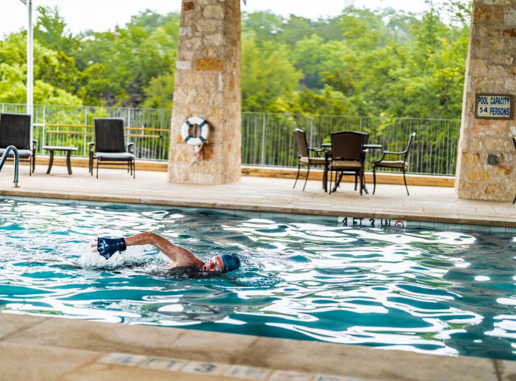 senior man in swim cap swims laps in the beautiful outdoor pool at Querencia Senior Living Community in Austin, TX