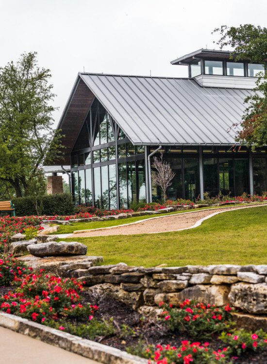 lush landscaping along a driveway leading up to the glass fitness building at Querencia Senior Living Community in Austin, TX