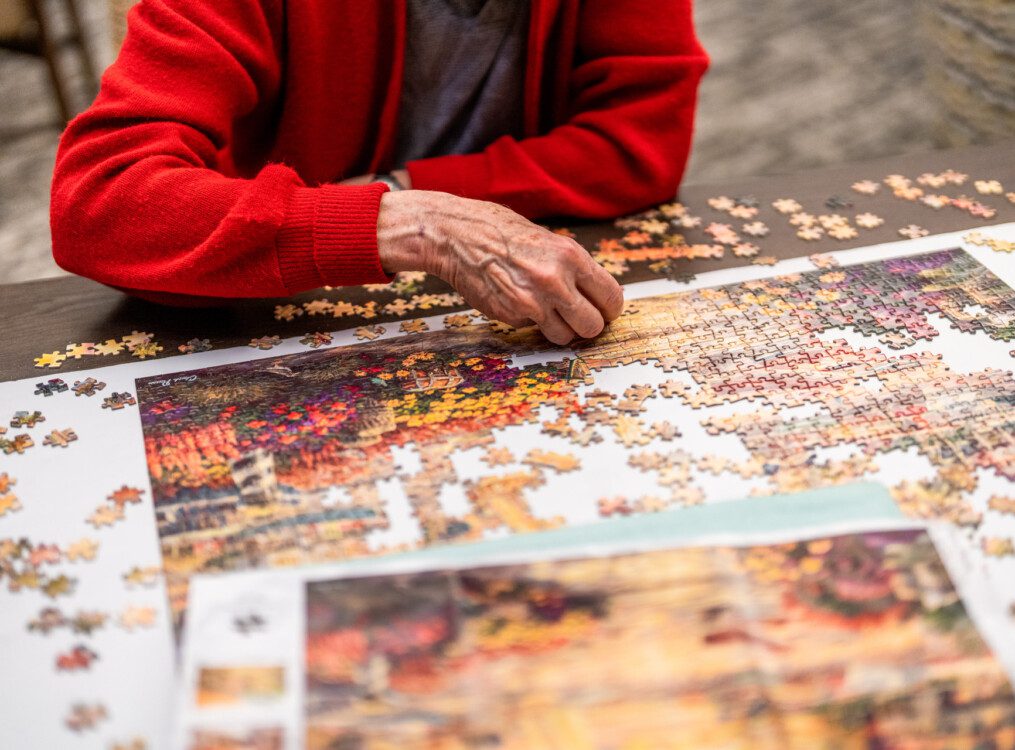 close-up of senior in red cardigan putting together a large puzzle