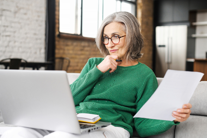 senior woman in green sweater sitting on her couch reviewing information on her laptop