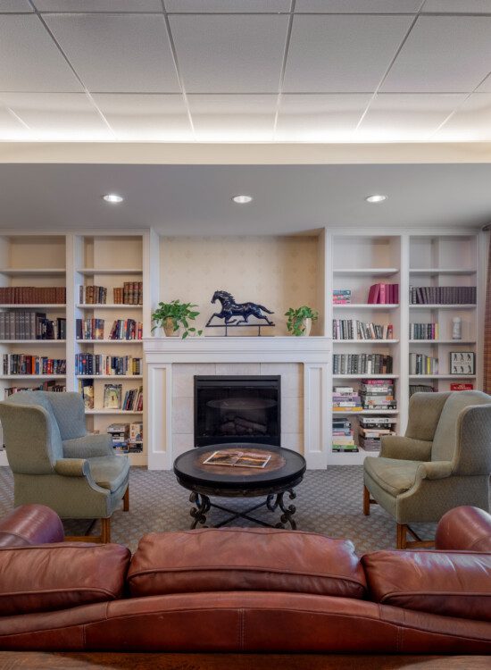 timeless community lounge with two large tufted chairs, a couch, and fireplace at Querencia's Assisted Living building